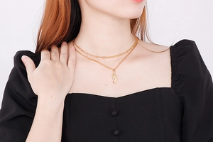 Detail of double-layer gold necklace featuring a leaf pendant on a fashion model