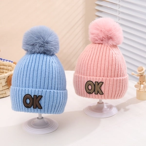 Detail view of pink and blue knit hats with large pom-poms and OK letter patches
