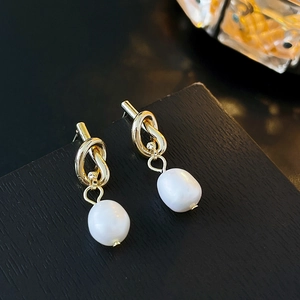 Gros plan de boucles d'oreilles nœuds dorés et perles baroques sur socle noir