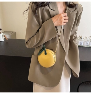 Close-up of a bright yellow apple-shaped crossbody bag with a gold chain strap on a model