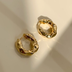 Detailansicht goldener Creolen mit unregelmäßiger Lavatextur und glänzendem Finish