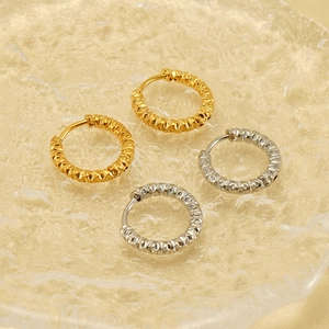 Boucles d'oreilles créoles martelées dorées et argentées sur un plateau en verre