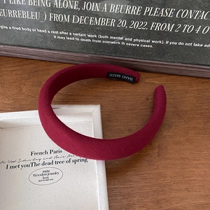 Close-up of thick burgundy corduroy headband with a handmade label on wooden table