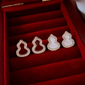 Détail de boucles d'oreilles gourde dorées avec pierres rouges et blanches et zircons