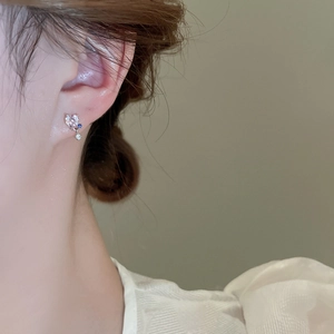 Detailed close-up of a silver heart earring with blue and white zircon stones on a model
