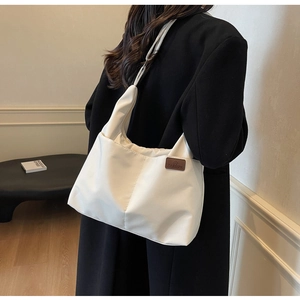Close-up of white tote bag side showing brown leather fashion tag on durable nylon fabric