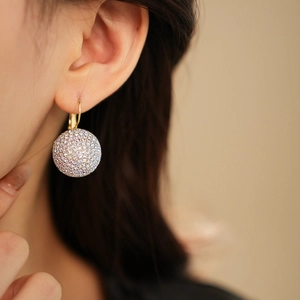 Close-up of a gold sphere earring with pavé crystals worn on a model's ear