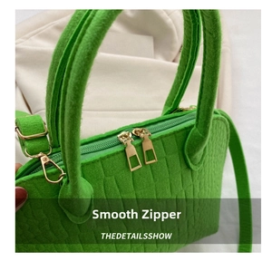 Detail of smooth double gold zippers on a green stone textured felt seashell bag