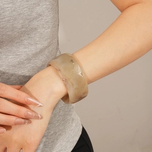 Detail view of a wide marble-patterned resin bangle worn on a model's wrist