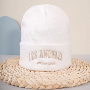 Détail de la broderie dorée LOS ANGELES sur un bonnet en maille blanche douce
