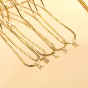 Flat lay of gold snake chain necklaces with crystal letter pendants A B K P R