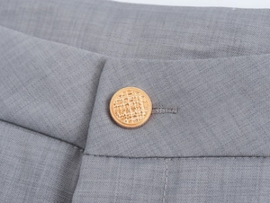 Détail de la taille en tissu gris avec un bouton en métal doré texturé sur le pantalon