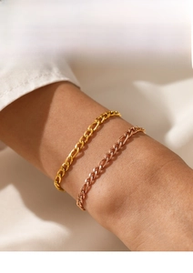 Detail of gold and rose gold Figaro chain bracelets on wrist over white fabric
