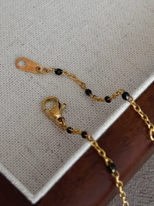 Macro detail of gold-plated stainless steel chain with black beads and lobster clasp