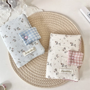 Close-up of floral fabric book covers with heart buttons and plaid strap on woven mat