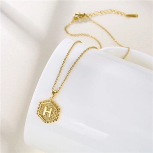 Close-up of golden hexagonal pendant with letter H and grainy texture on white ceramic