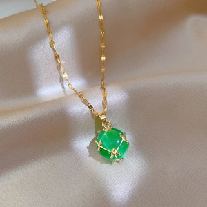 Makroaufnahme der goldenen Kette mit grünem Würfelanhänger auf Seidenhintergrund