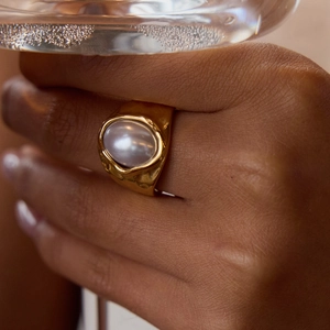 Elegant 18K gold plated hammered ring with white pearl on a model's hand holding a glass