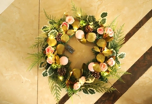 Detail of Christmas wreath with pink roses, pine cones, gold leaves and warm LED lights