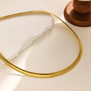 Detailed macro shot of flat gold snake bone chain necklace over decorative stone