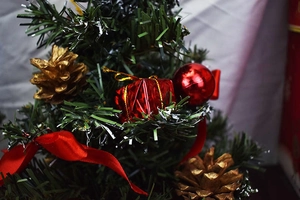 Close-up of artificial mini Christmas tree with gold pine cones and red ribbon ornaments