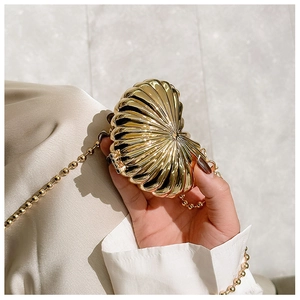 Detailed close-up of a mini gold shell-shaped clutch with radiant ribbed texture and bead chain