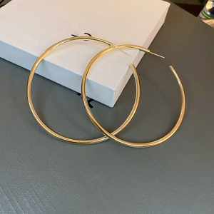 Detailed view of large gold hoop earrings on a textured jewelry box with polished finish