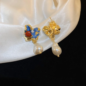 Macro detail of irregular golden earrings featuring enamel drips and baroque pearls