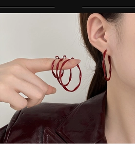Detailed view of dark red twisted hoop earrings with a glossy retro finish and curved design