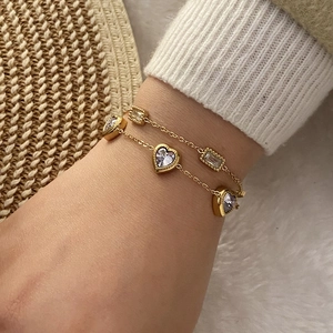 Détail d'un bracelet doré double couche avec cristaux de cœur violets sur un poignet