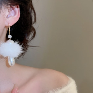 Detail showing a C-shaped earring with soft white fur ball and elegant pearl teardrop