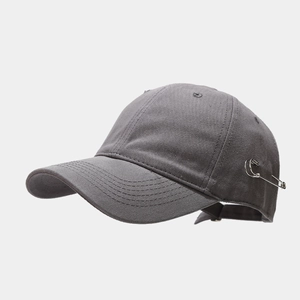Close-up of a dark grey baseball cap with silver safety pin and metal rings detail