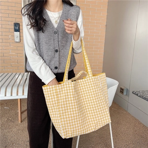 Detail of yellow checkered tote bag held by a model against a warm brick wall background