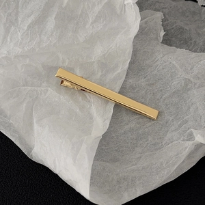 Detailed close-up of a polished gold minimalist rectangular metal hair clip on a textured base