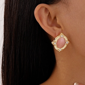 Close-up of vintage gold earrings with pink cat-eye stone and rhinestones worn by a model