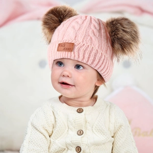 Detail of pink baby knit hat with double brown fur pom-poms and warm textured cable knit