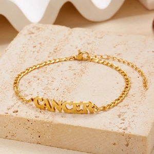 Gold-plated stainless steel Cancer zodiac charm bracelet on a textured stone display