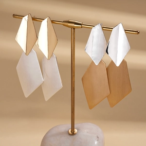 Minimalist geometric rhombus earrings in gold and silver finish on a display stand