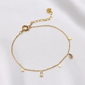 Gold chain bracelet with water drop zircon charms and metal discs on white satin background