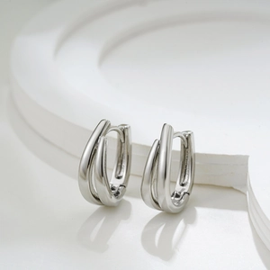 Close-up of minimalist silver triple-layered overlapping hoop earrings on white stone stand