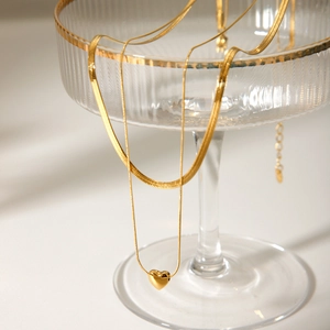 Double-layered 18k gold snakeskin chain necklace with a heart pendant on glass tray