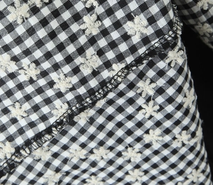 Macro shot of black and white plaid fabric with small white floral embroidery detail