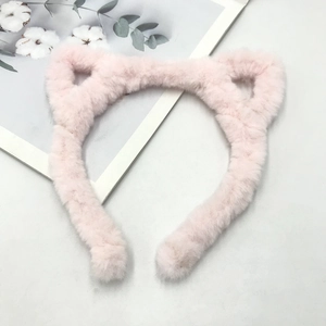 Top-down view of a soft plush pink cat ear headband on a decorative light gray surface