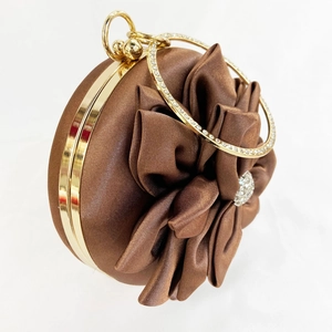 Close-up of brown satin evening bag featuring a pleated flower and rhinestone handle