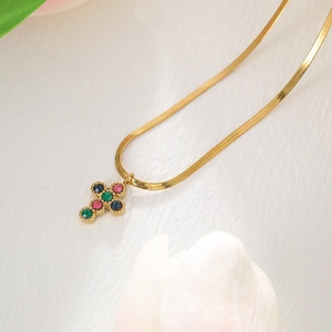 Detail view of a gold stainless steel cross necklace with colorful gems on a snake chain