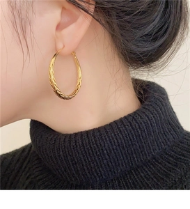 Close-up of gold twisted hoop earrings with woven metal texture worn by a model