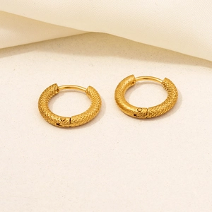 Detailed view of gold hoop earrings with snake scale texture on a cream fabric surface