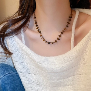 Vue détaillée d'un collier en perles d'oeil de tigre sur un pull en tricot blanc