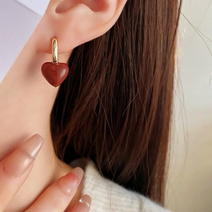Close-up of a model wearing a gold U-shaped hoop earring with a red heart pendant
