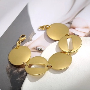 Dettaglio del bracciale a catena dorato con maglie circolari su un vassoio di ceramica bianca